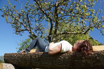 Foto einer Frau die sich eine Auszeit auf einem Baumstamm am Karnerhof gönnt