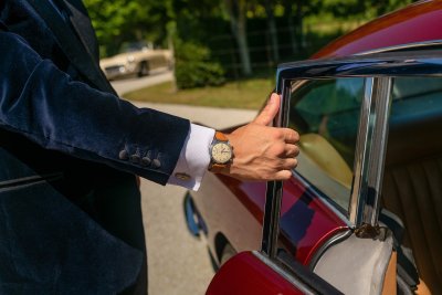 Foto eines Aston Martins mit Person die mit einer schönen Uhr die Tür öffnet